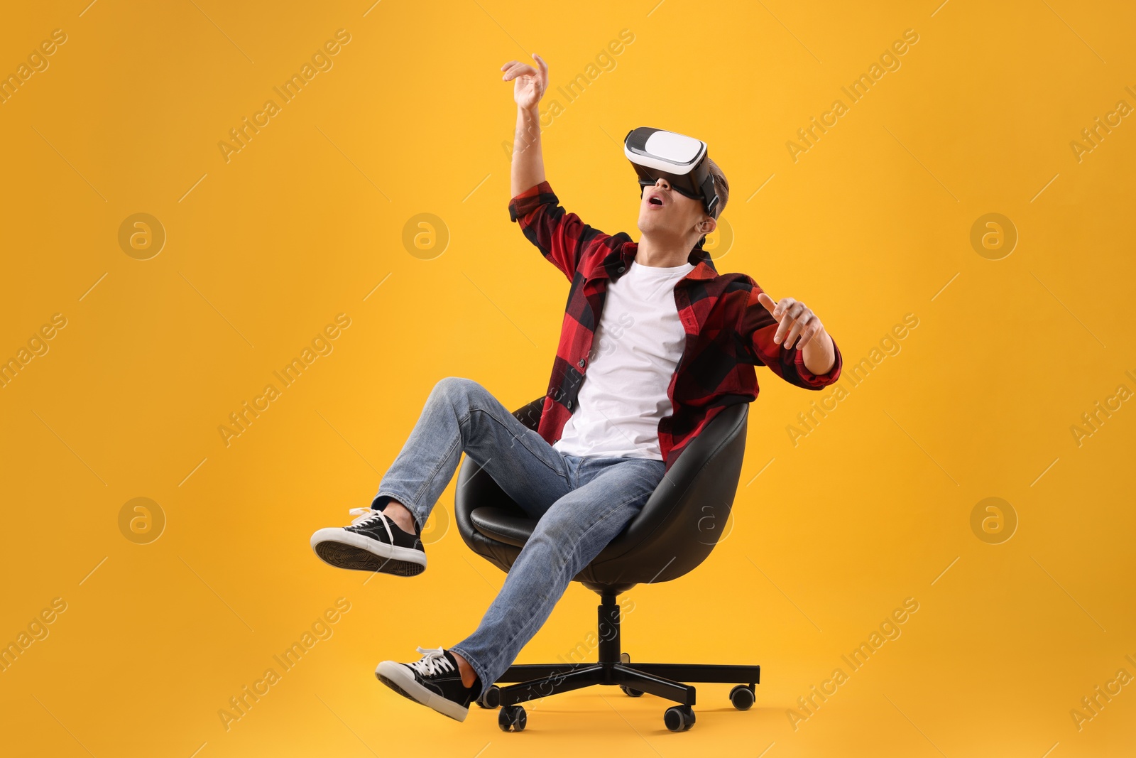 Photo of Emotional young man with virtual reality headset sitting on chair against yellow background