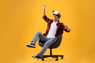 Emotional young man with virtual reality headset sitting on chair against yellow background