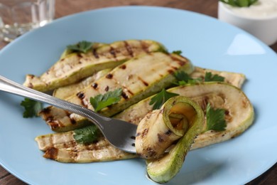 Photo of Eating tasty grilled courgette slices at table, closeup