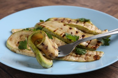 Eating tasty grilled courgette slices at wooden table, closeup