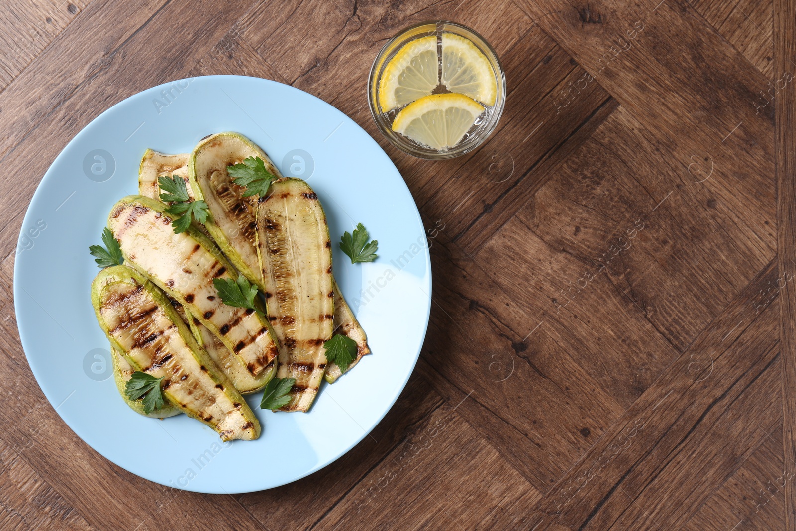 Photo of Tasty grilled courgette slices with parsley served on wooden table, flat lay. Space for text