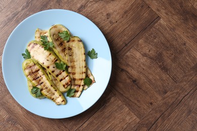 Photo of Tasty grilled courgette slices with parsley on wooden table, top view. Space for text