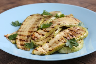 Tasty grilled courgette slices with parsley on wooden table, closeup