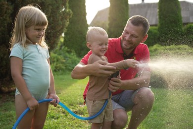 Photo of Little boy watering lawn with hose while his father and sister watching in backyard