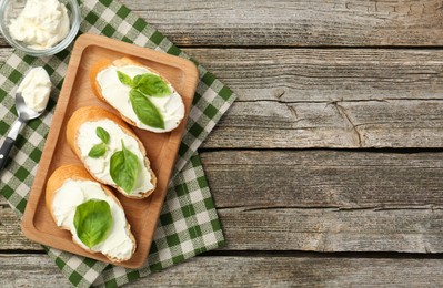 Delicious sandwiches with cream cheese and basil leaves on wooden table, top view. Space for text