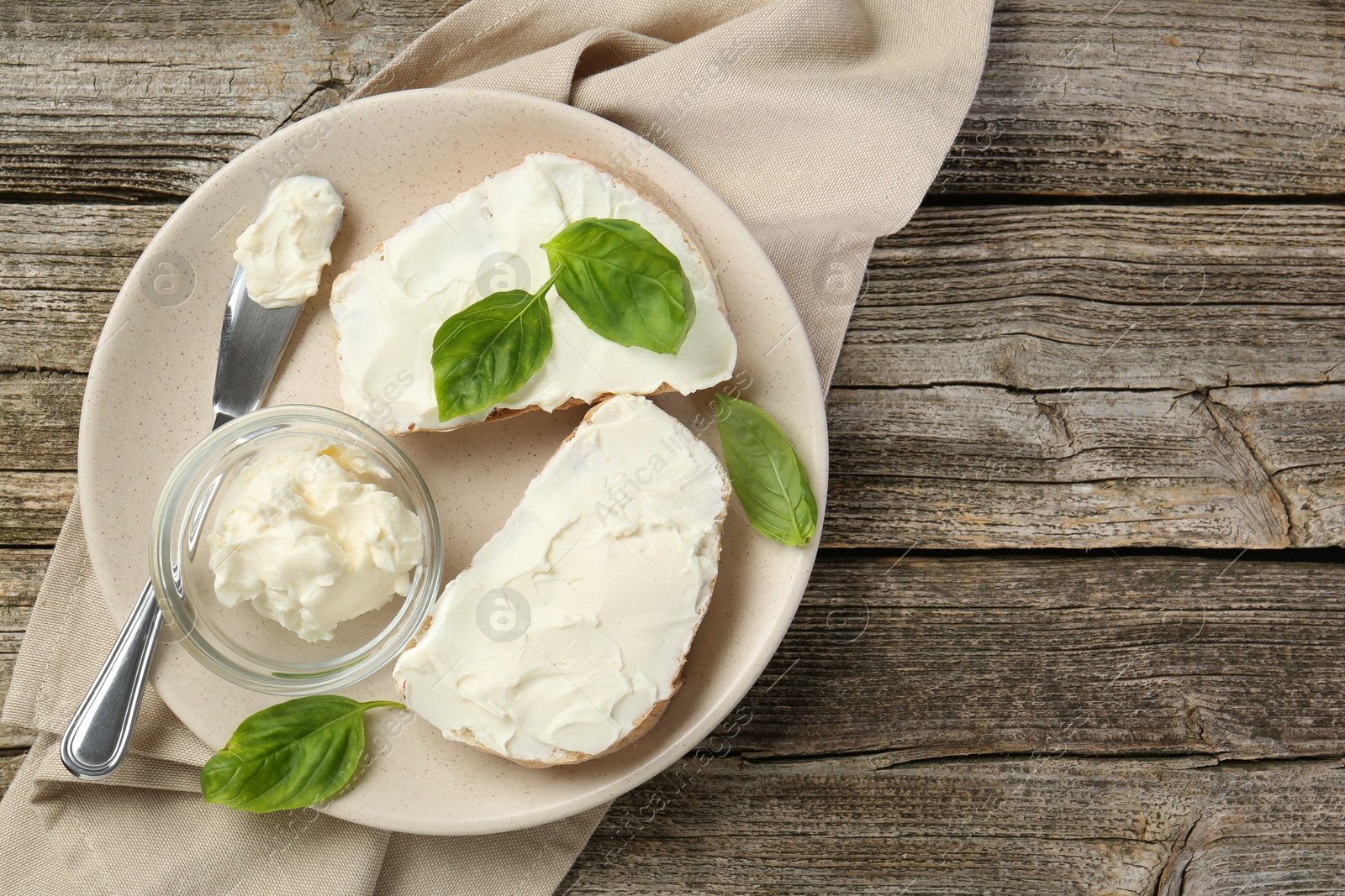 Photo of Delicious sandwiches with cream cheese and basil leaves on wooden table, top view. Space for text