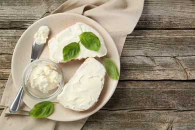 Delicious sandwiches with cream cheese and basil leaves on wooden table, top view. Space for text