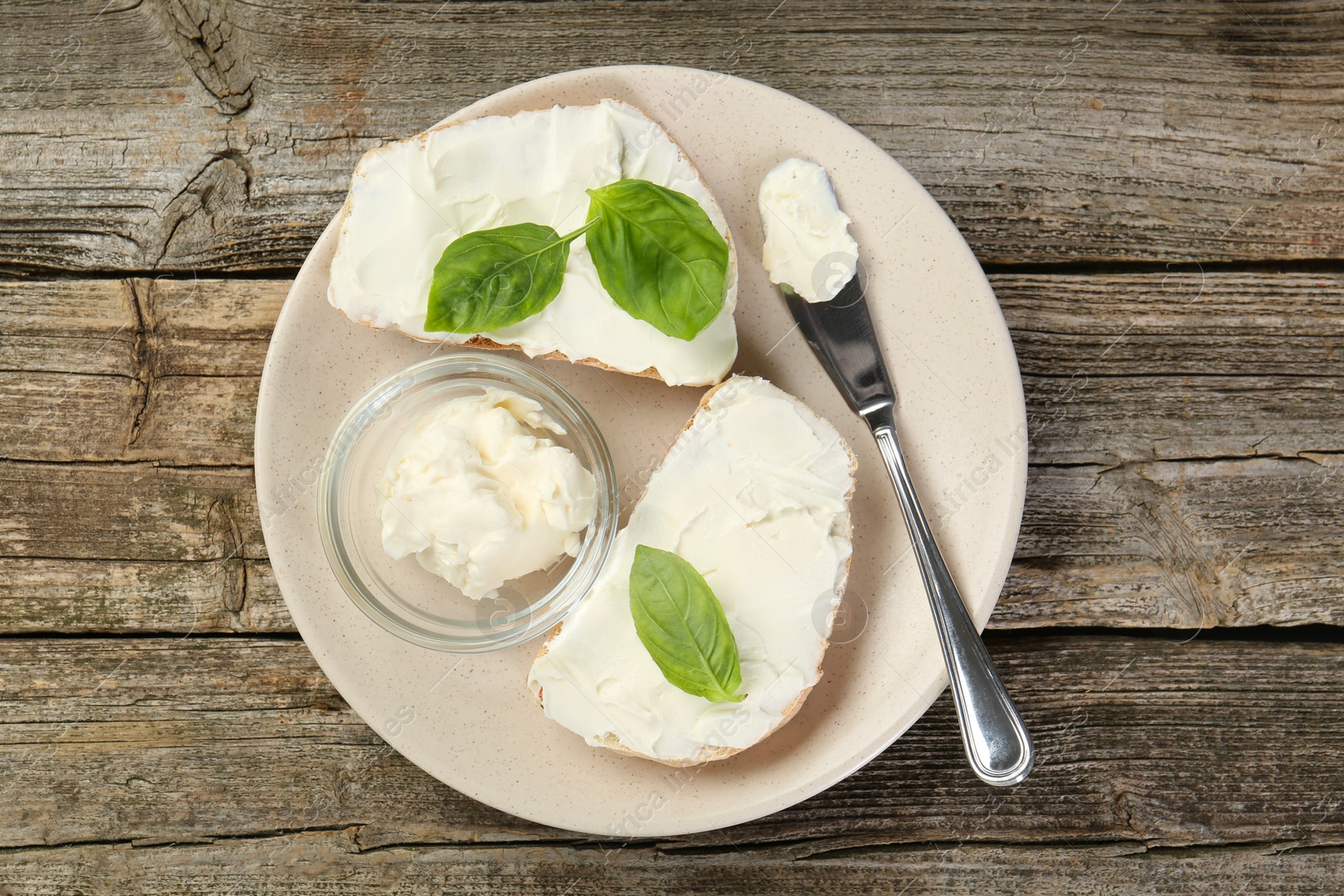 Photo of Delicious sandwiches with cream cheese and basil leaves on wooden table, top view