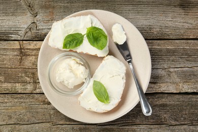 Delicious sandwiches with cream cheese and basil leaves on wooden table, top view