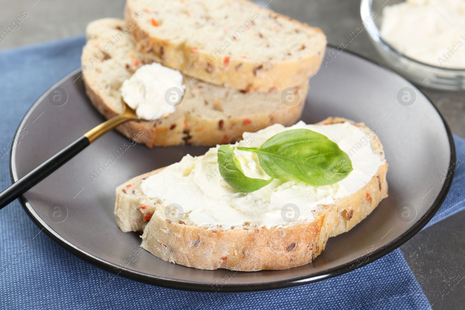 Photo of Pieces of bread with cream cheese and basil leaves on gray table, closeup