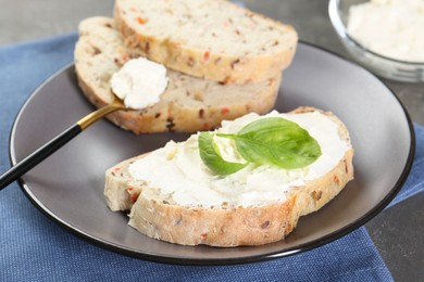 Pieces of bread with cream cheese and basil leaves on gray table, closeup