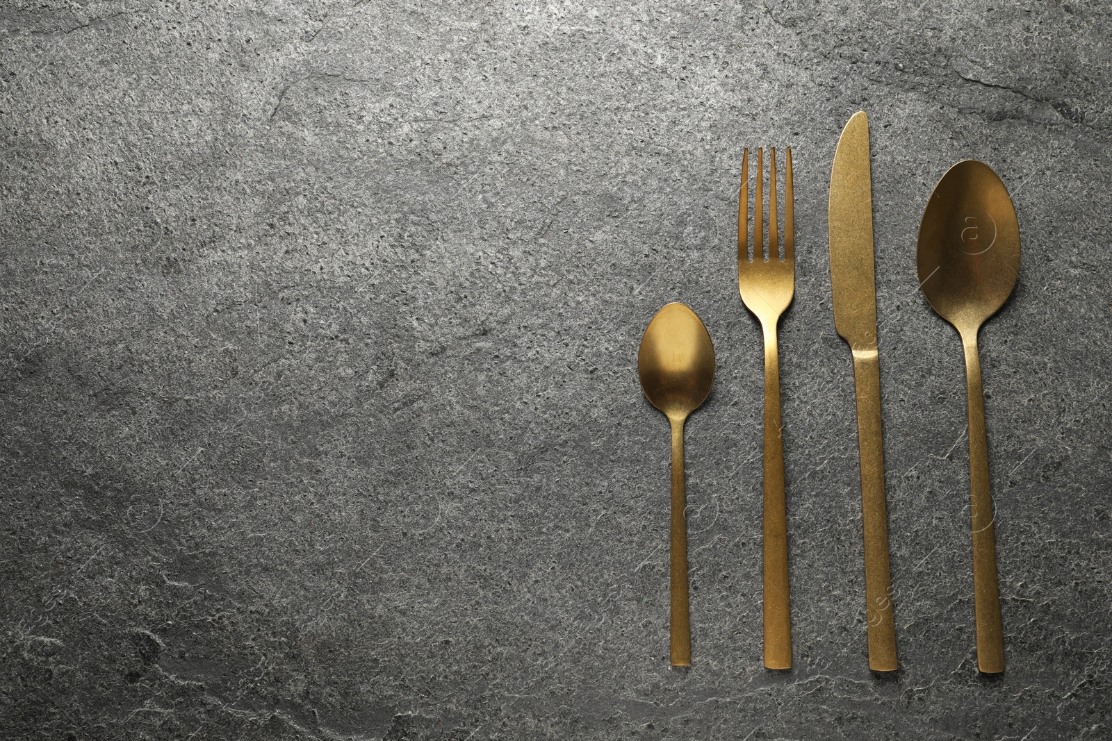 Photo of Stylish golden cutlery on grey table, flat lay. Space for text