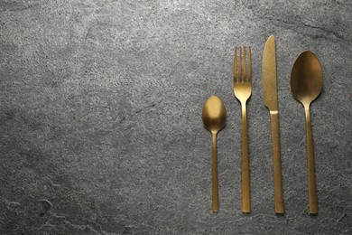 Photo of Stylish golden cutlery on grey table, flat lay. Space for text