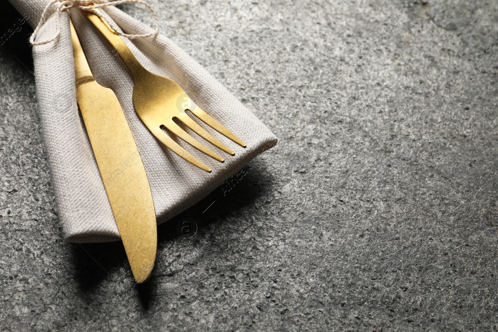 Photo of Stylish golden cutlery and napkin on grey table, closeup. Space for text