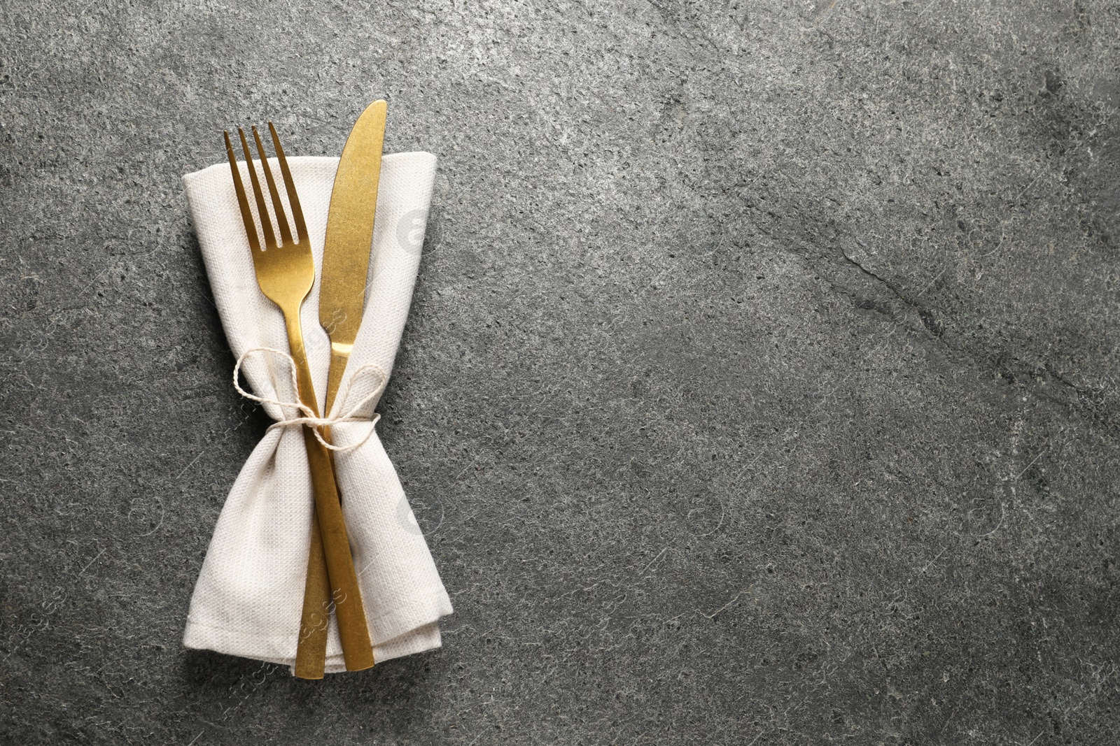 Photo of Stylish golden cutlery and napkin on grey table, top view. Space for text