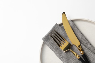 Photo of Stylish golden cutlery, plate and napkin on white background, top view. Space for text