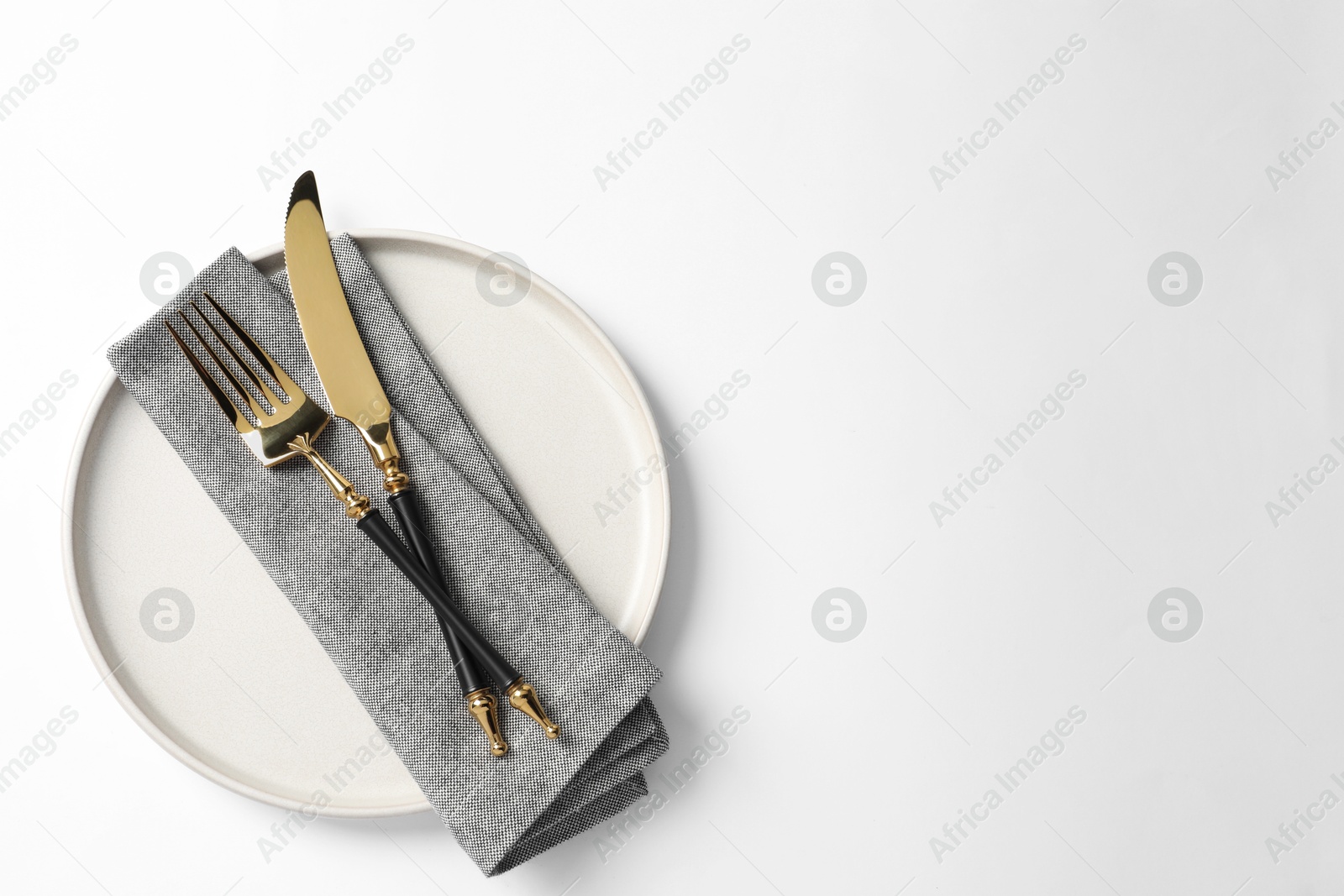 Photo of Stylish golden cutlery, plate and napkin on white background, top view. Space for text