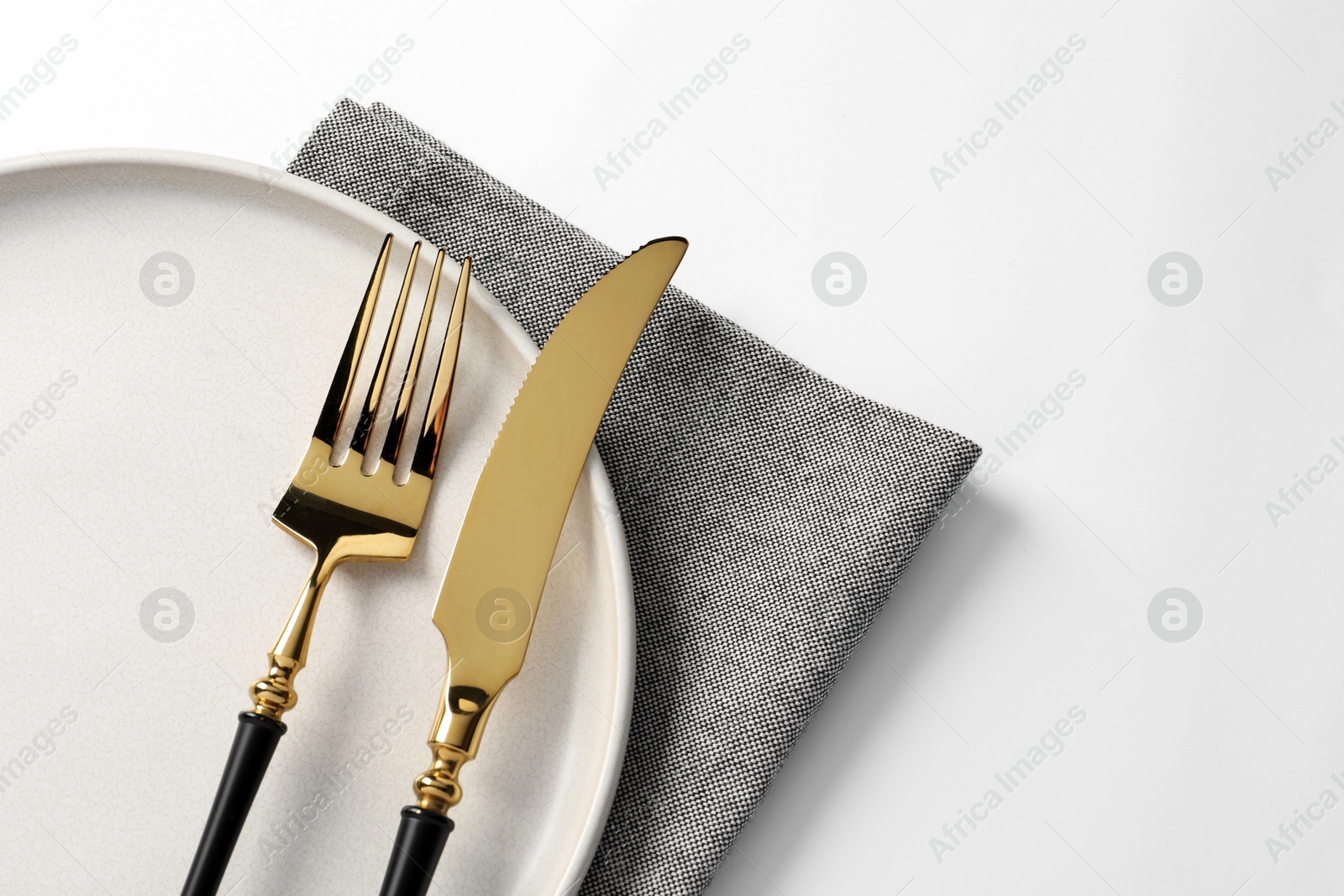 Photo of Stylish golden cutlery, plate and napkin on white background, top view. Space for text