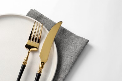 Photo of Stylish golden cutlery, plate and napkin on white background, top view. Space for text