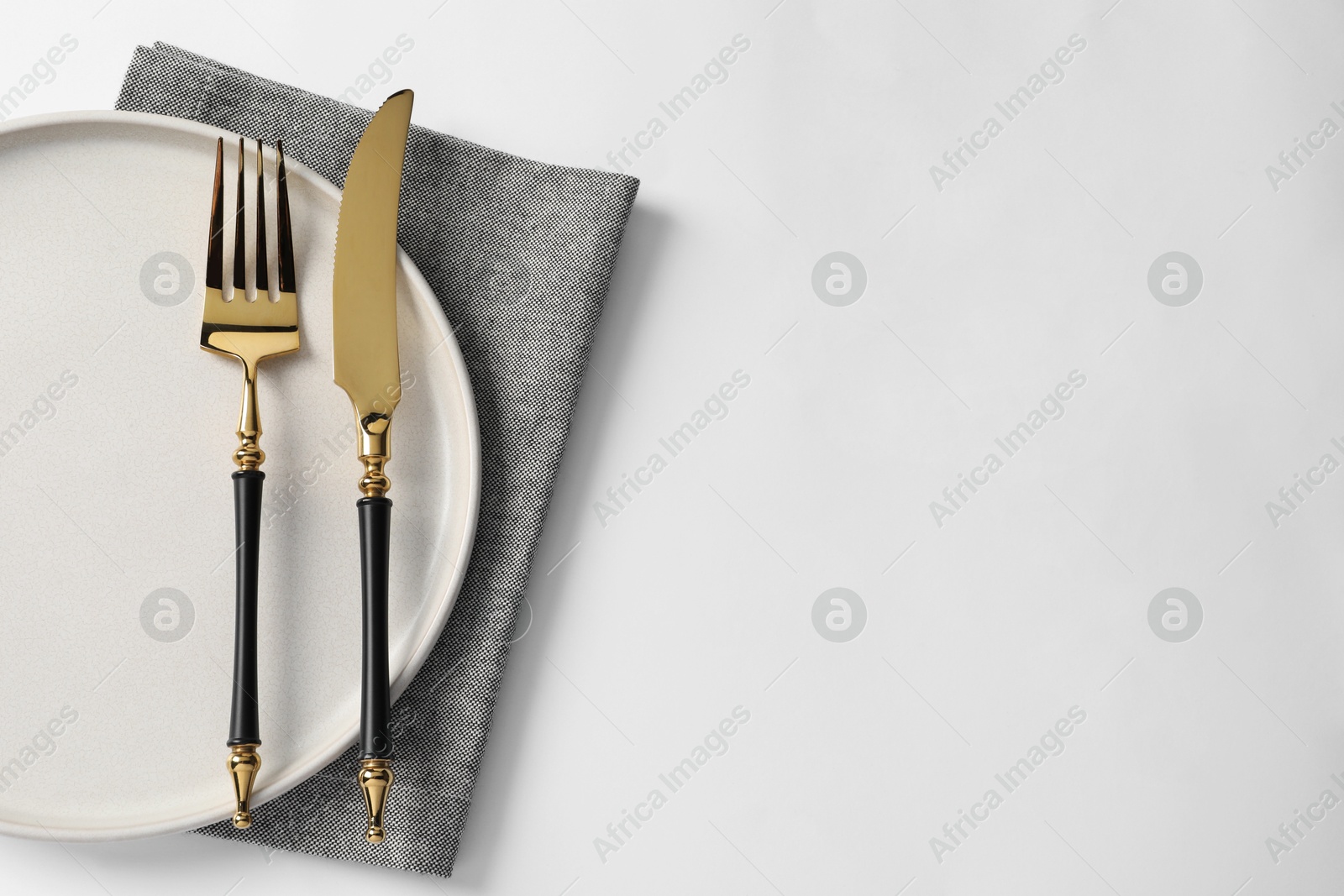 Photo of Stylish golden cutlery, plate and napkin on white background, top view. Space for text