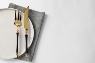 Stylish golden cutlery, plate and napkin on white background, top view. Space for text