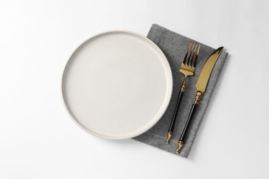 Stylish golden cutlery, plate and napkin on white background, top view