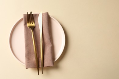 Photo of Stylish golden cutlery, plate and napkin on beige background, top view. Space for text