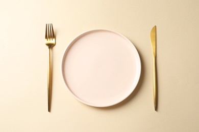 Photo of Stylish golden cutlery and plate on beige background, top view