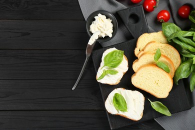 Pieces of bread with cream cheese and basil served on black wooden table, flat lay. Space for text