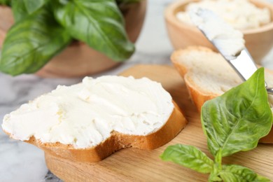 Photo of Pieces of bread with cream cheese and basil leaves on white table, closeup