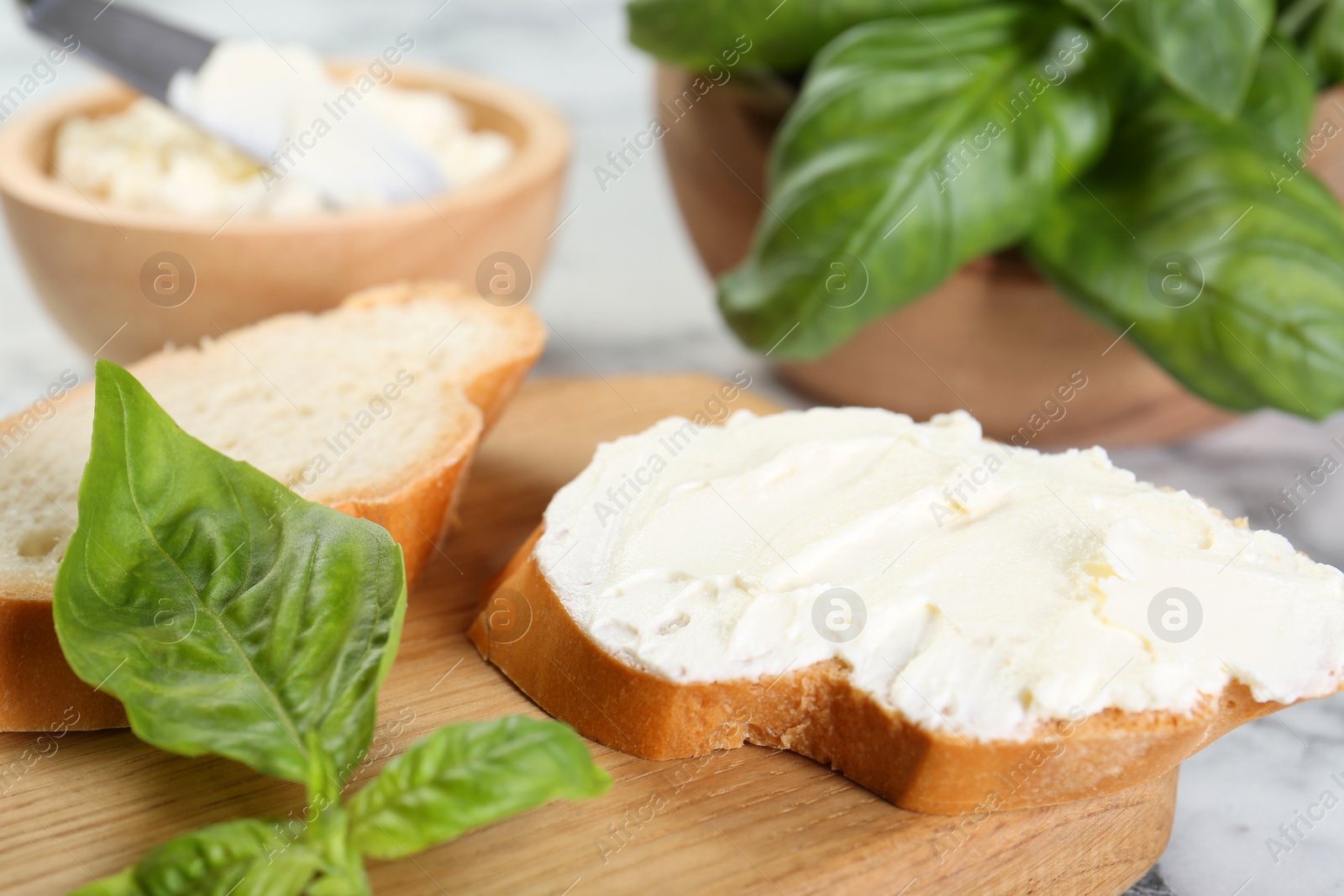 Photo of Pieces of bread with cream cheese and basil leaves on white table, closeup