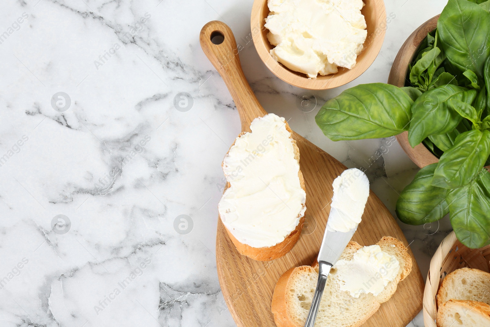 Photo of Pieces of bread with cream cheese and basil served on white marble table, flat lay. Space for text