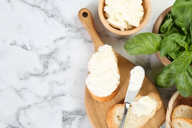 Pieces of bread with cream cheese and basil served on white marble table, flat lay. Space for text