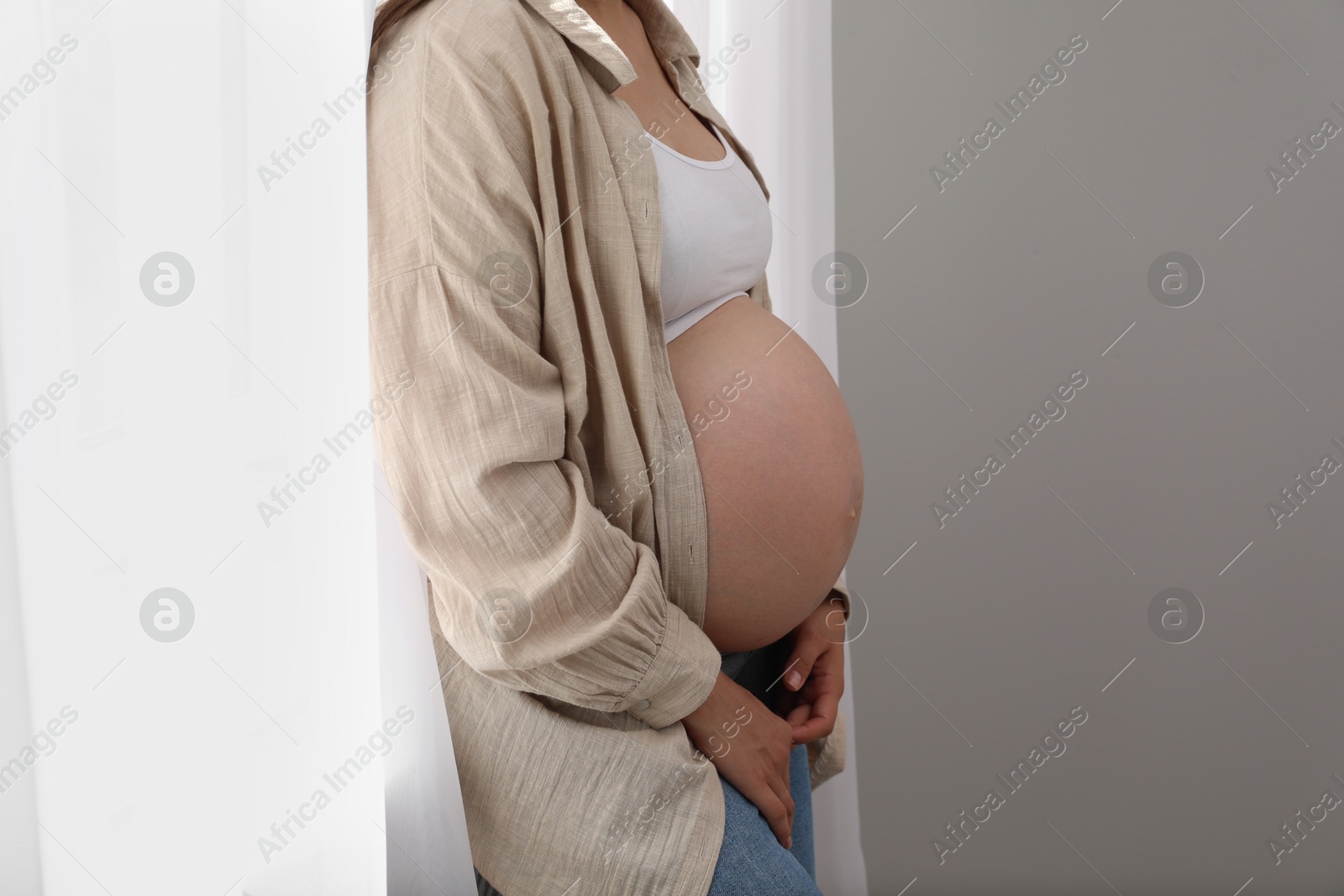 Photo of Pregnant woman near window at home, closeup