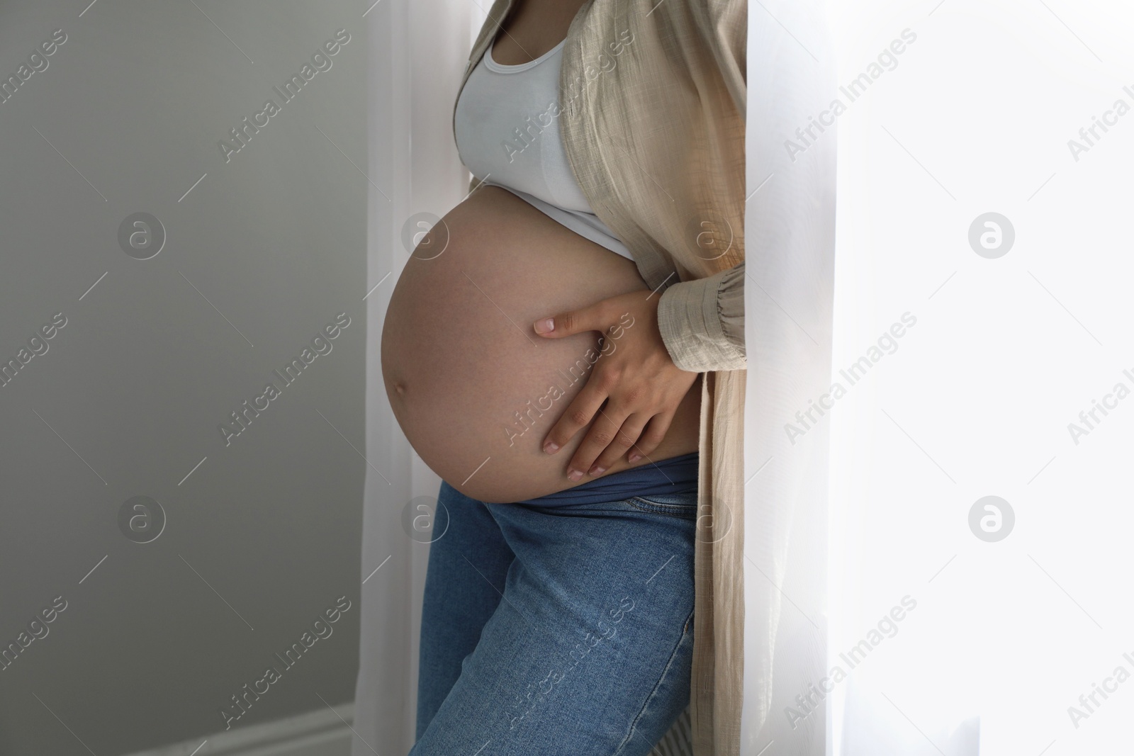 Photo of Pregnant woman near window at home, closeup