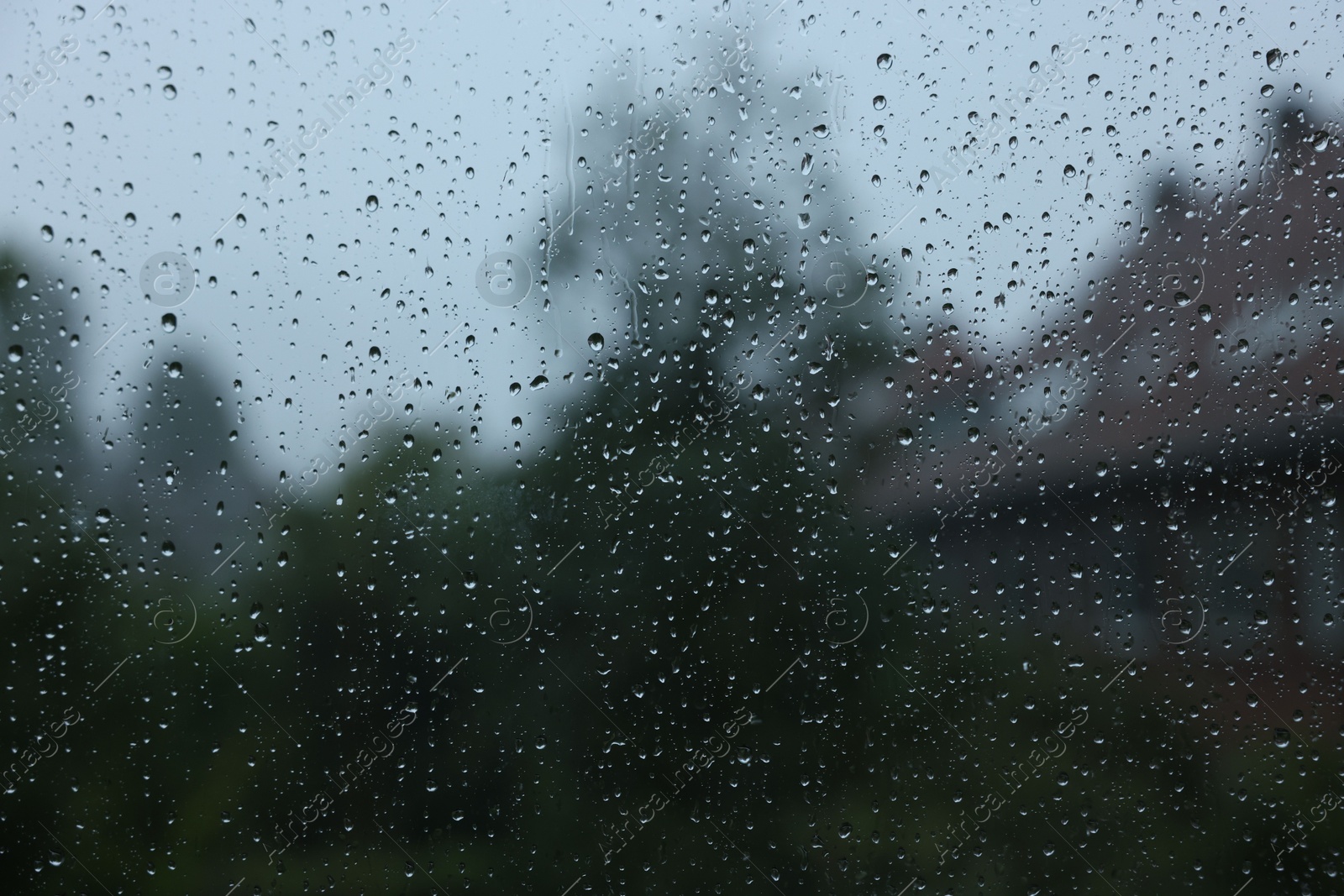 Photo of View on buildings through window with water droplets on rainy day, closeup