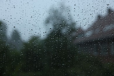 Photo of View on buildings through window with water droplets on rainy day, closeup