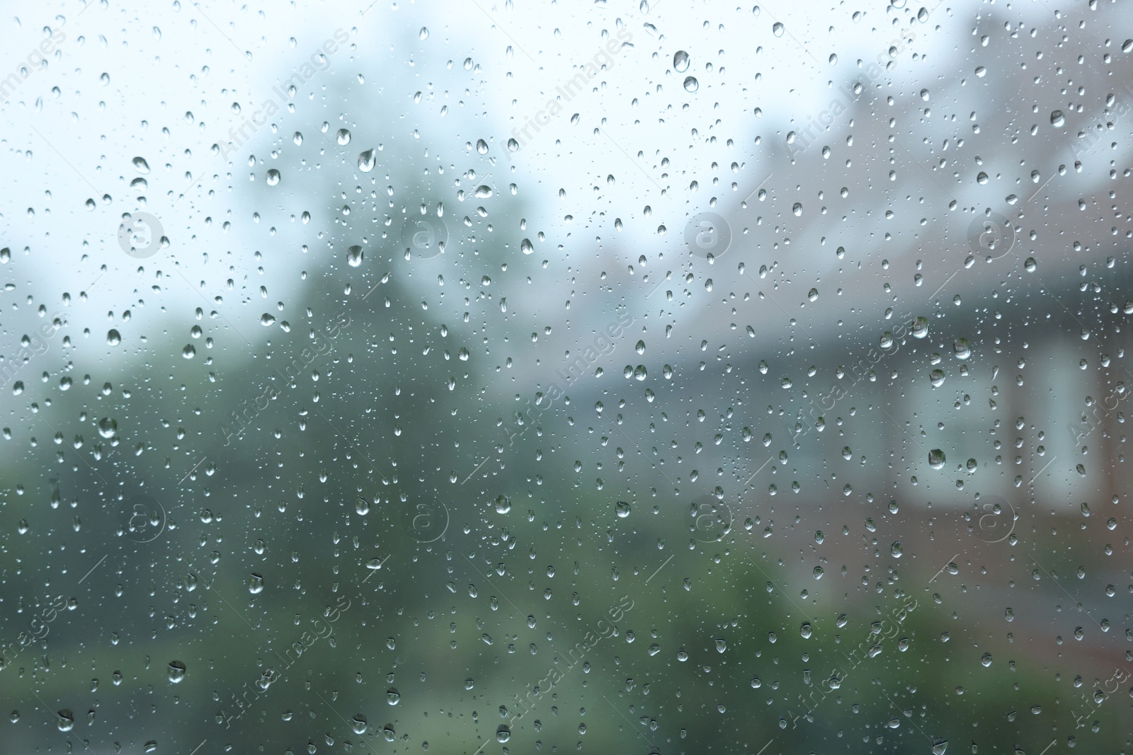 Photo of View on buildings through window with water droplets on rainy day, closeup