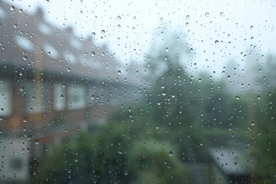 View on buildings through window with water droplets on rainy day, closeup