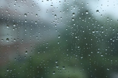 View on buildings through window with water droplets on rainy day, closeup