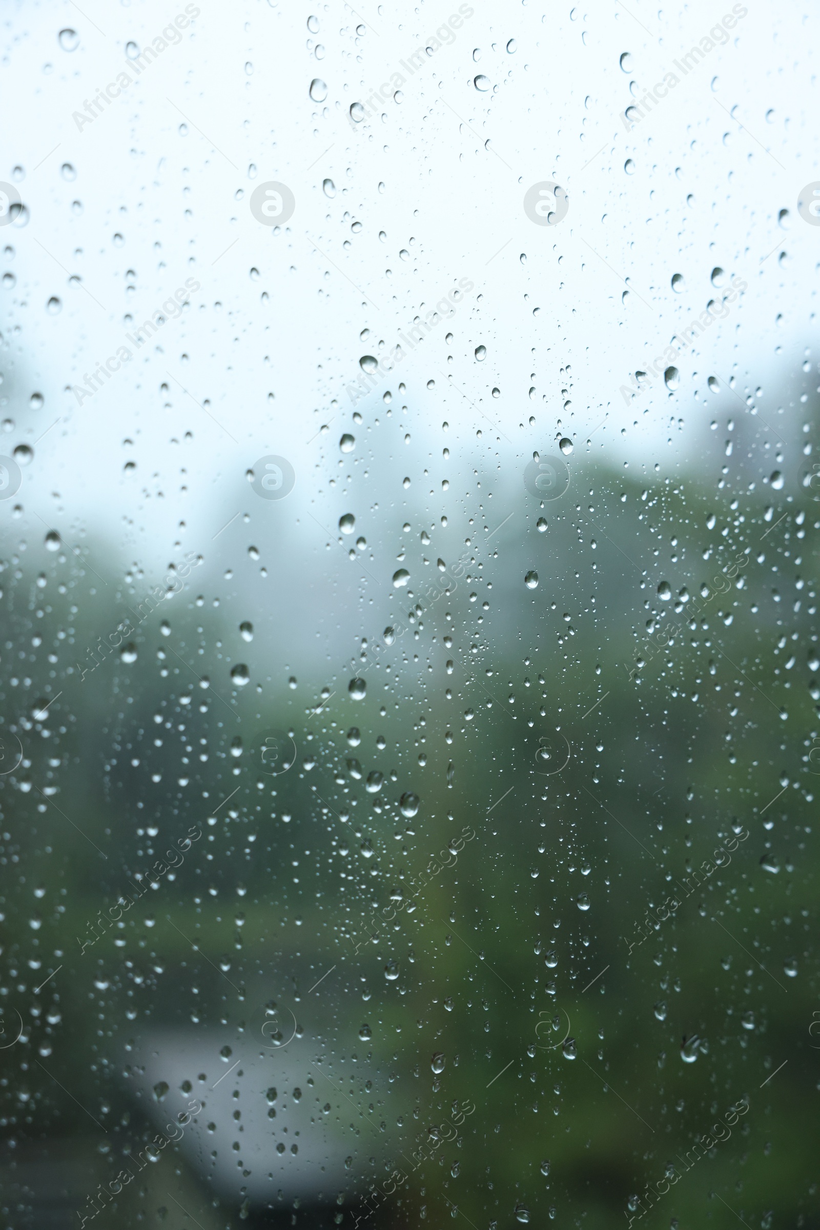 Photo of View on buildings through window with water droplets on rainy day, closeup