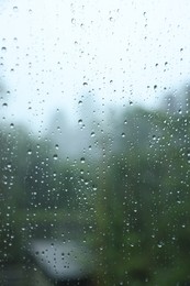 Photo of View on buildings through window with water droplets on rainy day, closeup