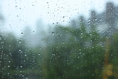 Photo of View on buildings through window with water droplets on rainy day, closeup