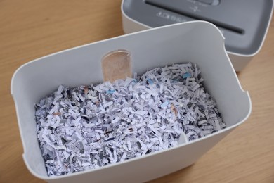 Shredder and basket with paper strips on wooden table, above view