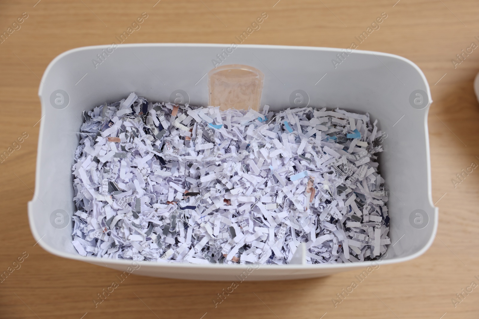 Photo of Shredded paper strips in bin on wooden table, top view