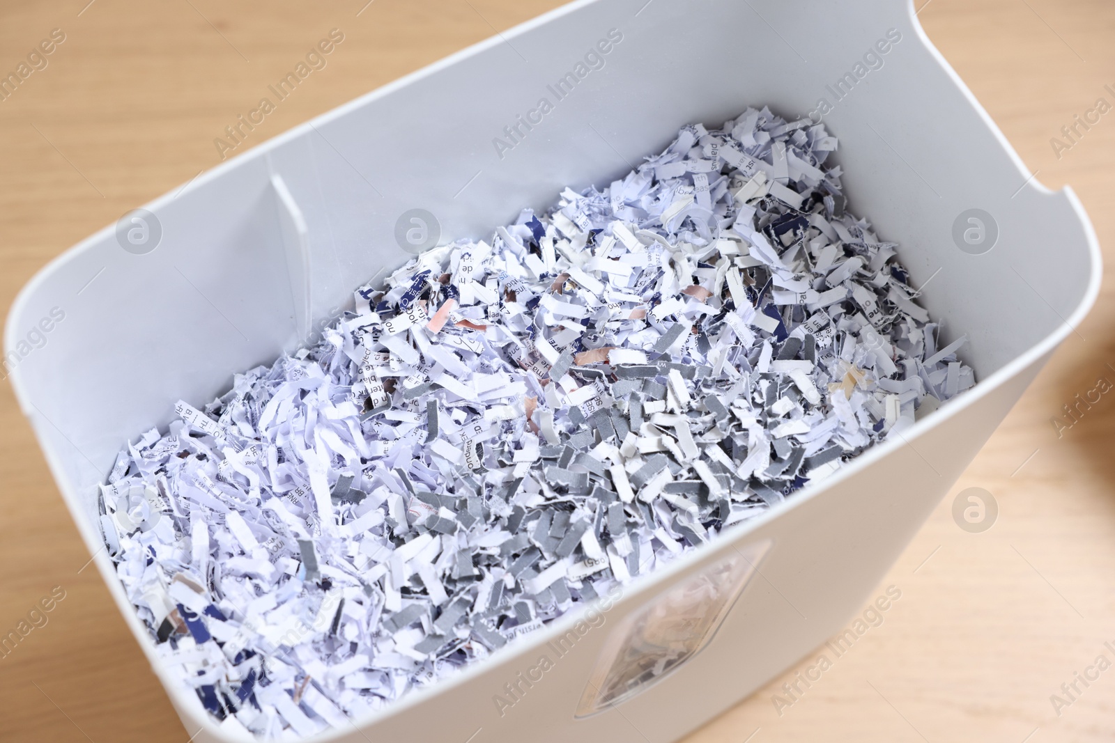 Photo of Shredded paper strips in bin on wooden table, closeup