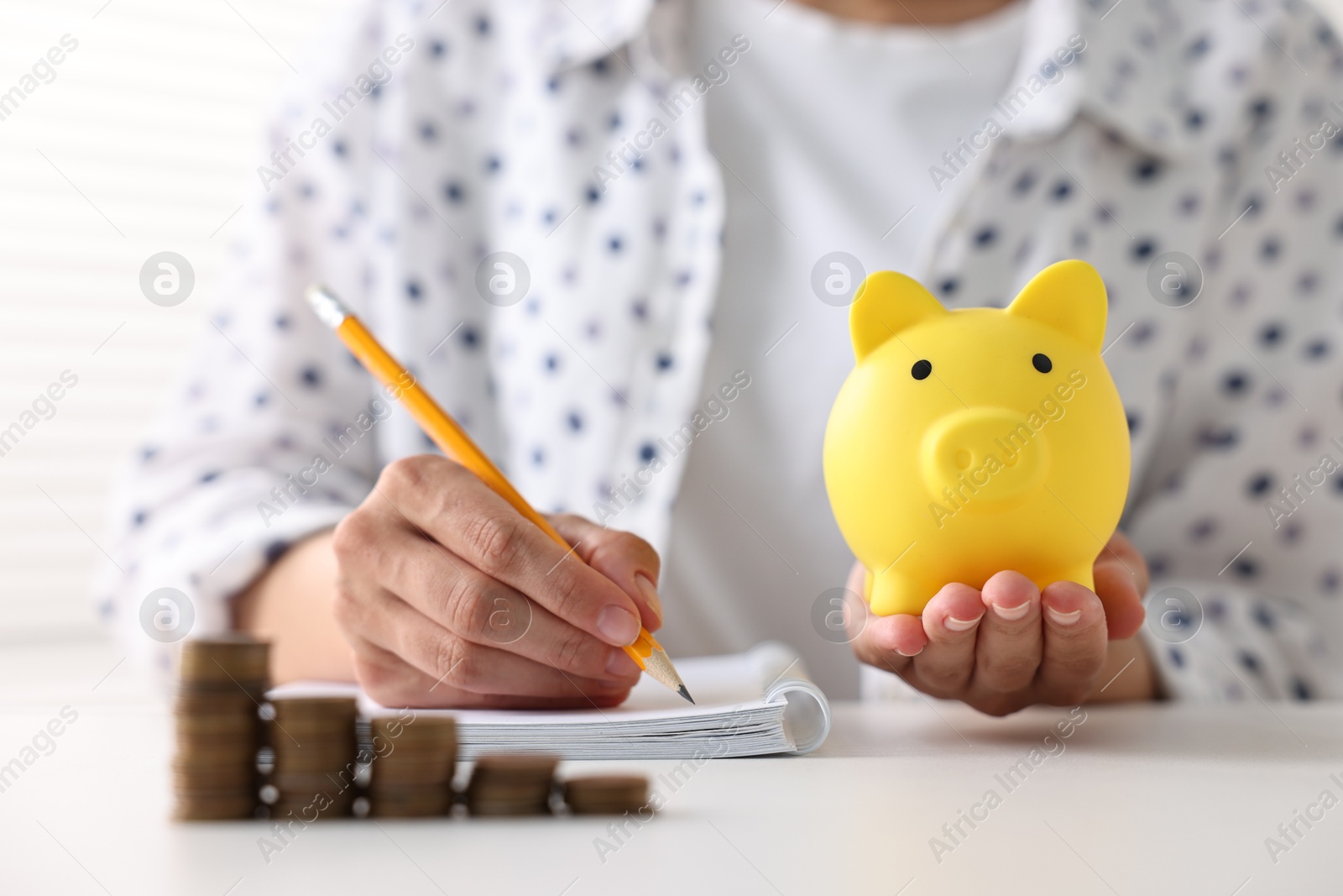 Photo of Woman with piggy bank taking notes and coins on table indoors, closeup