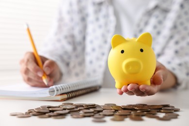 Photo of Woman with piggy bank taking notes and coins on table indoors, closeup