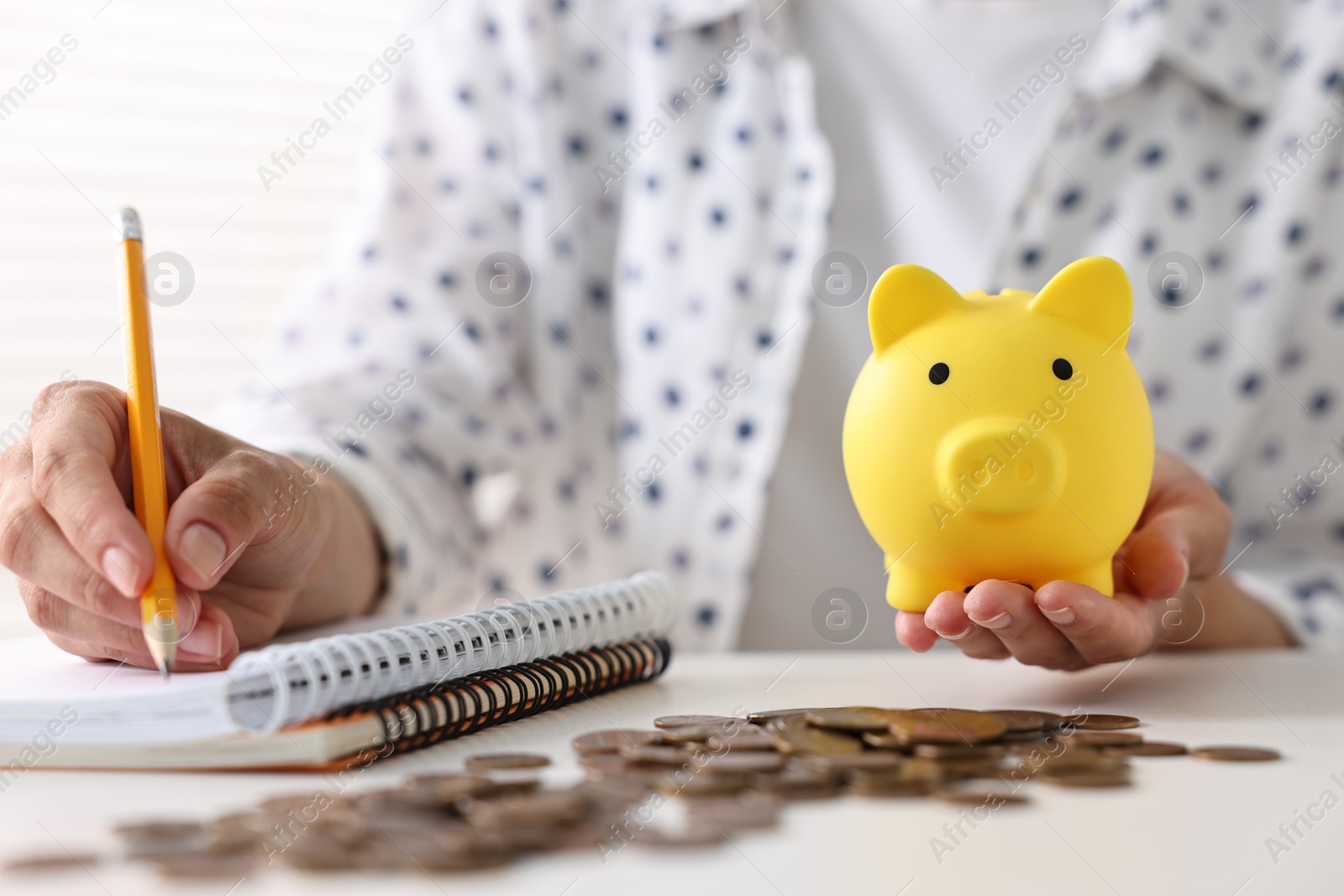 Photo of Woman with piggy bank taking notes and coins on table indoors, closeup