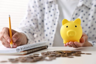 Photo of Woman with piggy bank taking notes and coins on table indoors, closeup